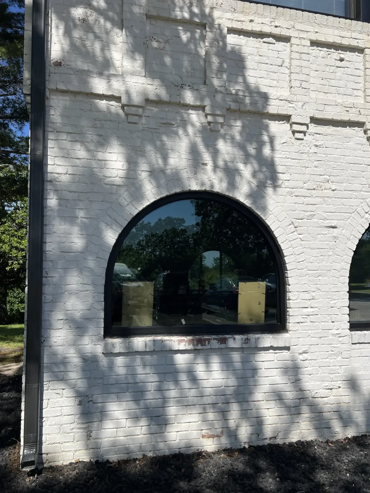 Arched black replacement window set into painted white brick
