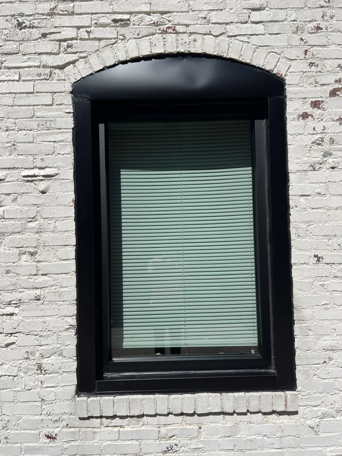 Close-up of a black-framed window installed in white brick