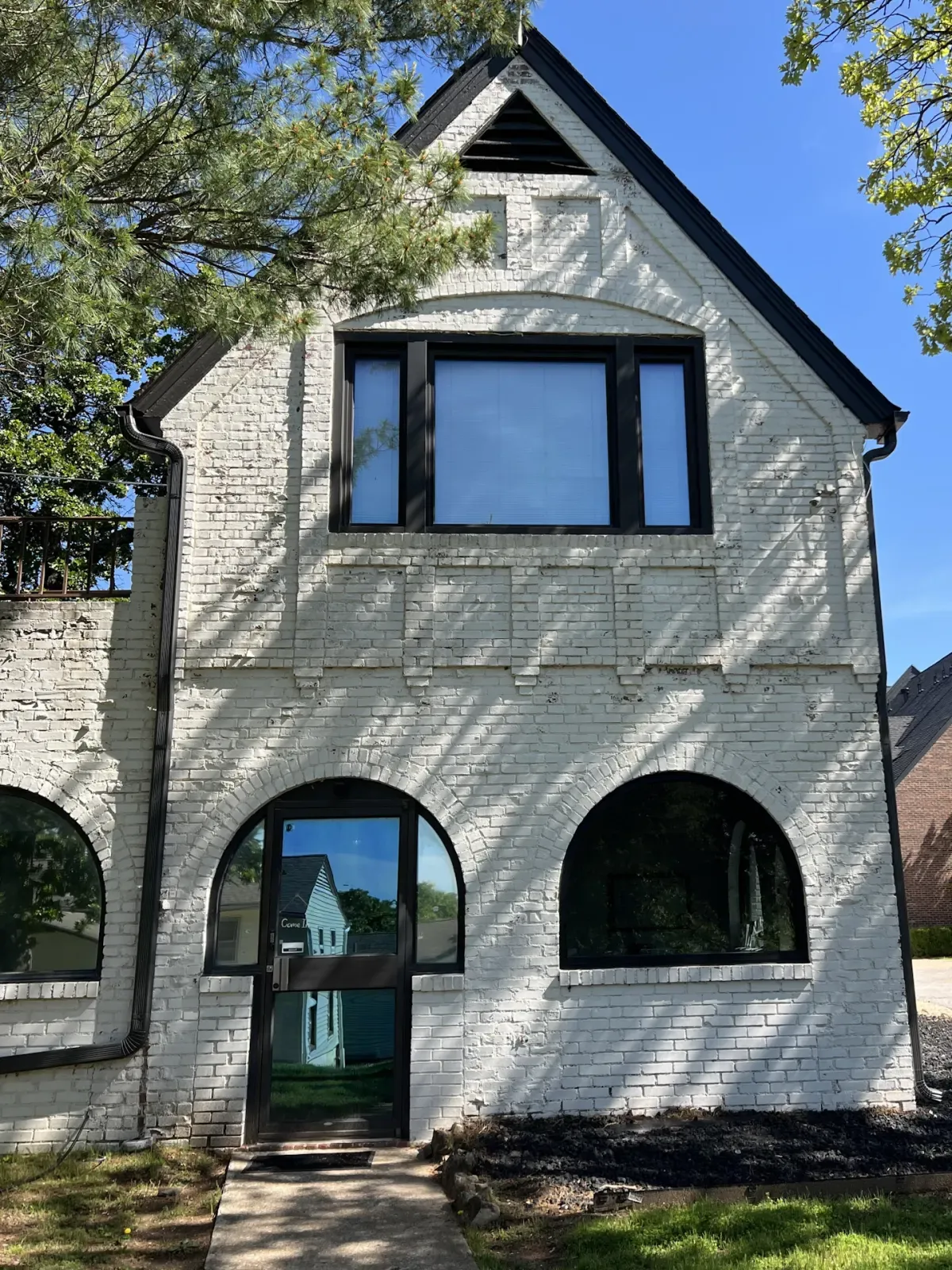 Arched black replacement windows in the gable of a painted white brick home