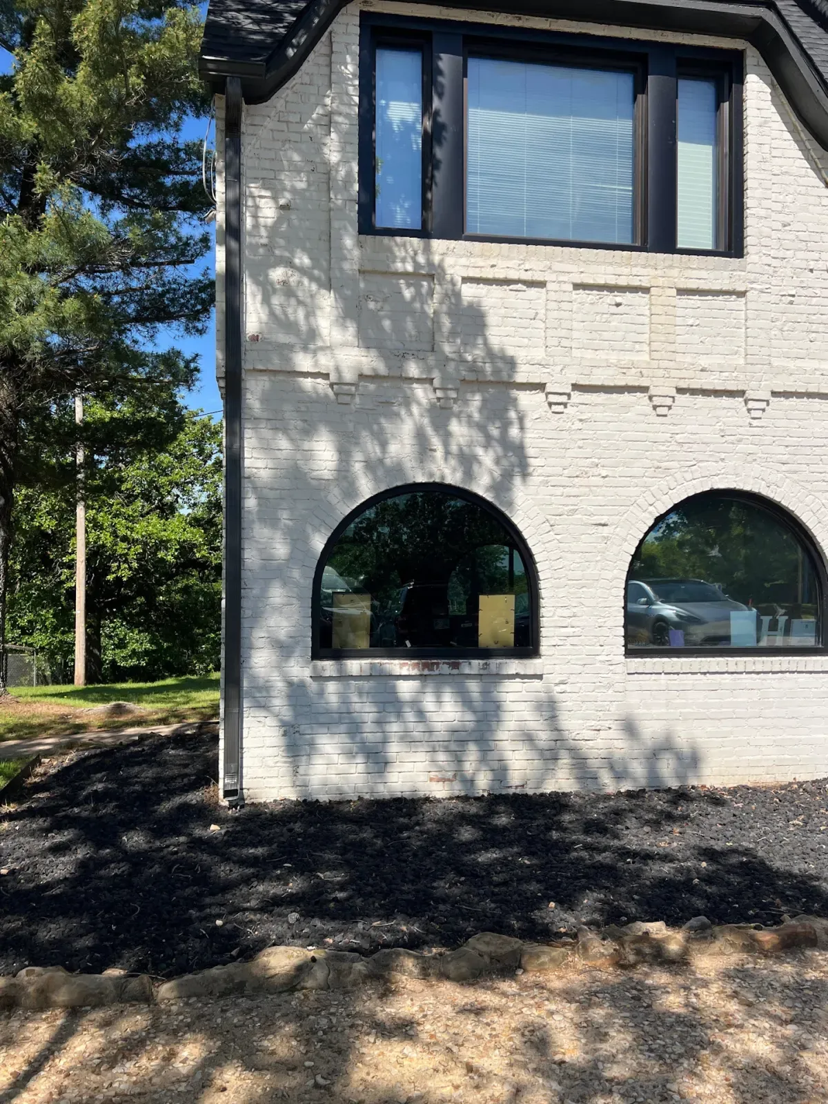 Pair of arched black-frame windows installed on a white brick home